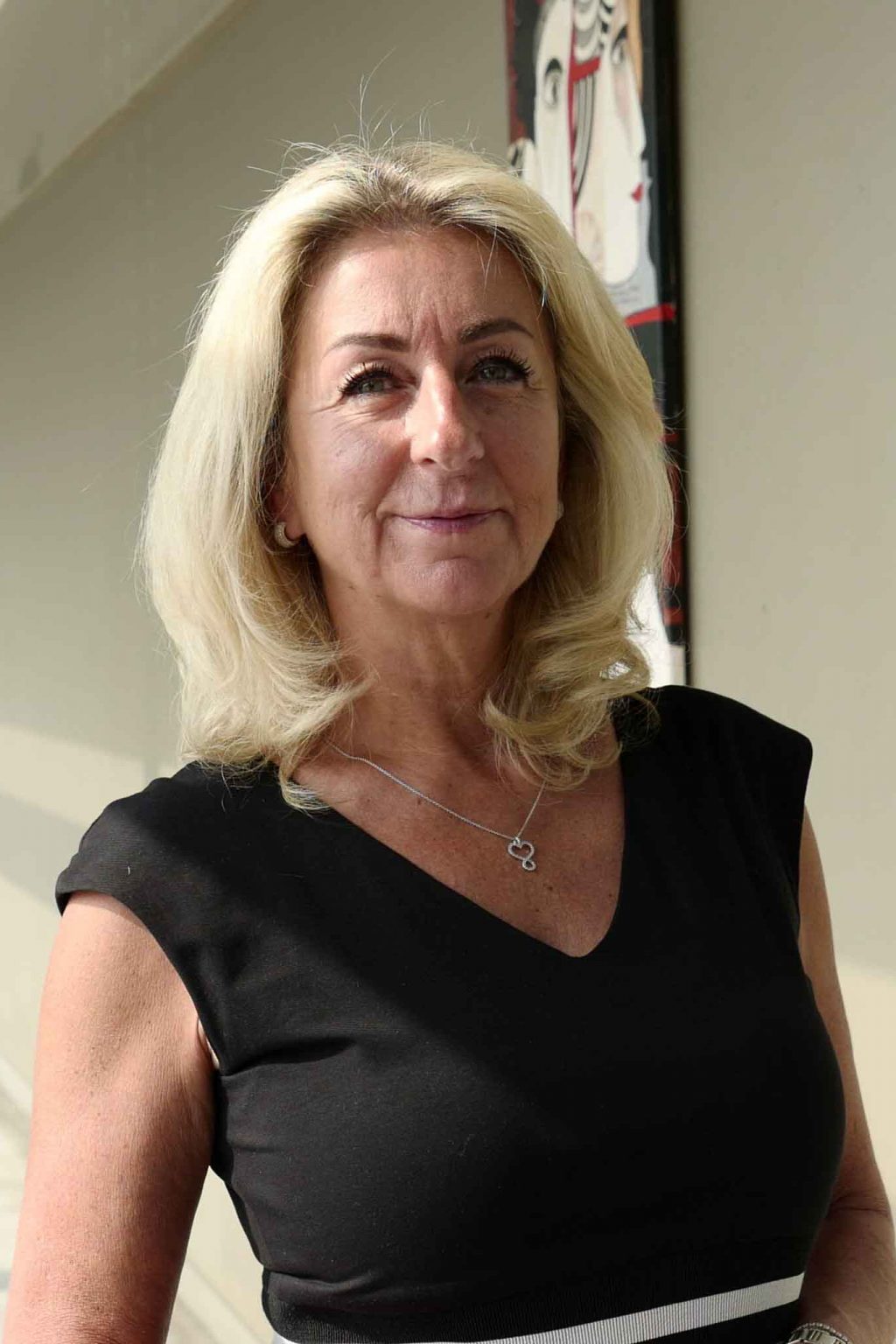 Elegante Frau in dunkler Bluse mit blondem, schulterlangem Haar